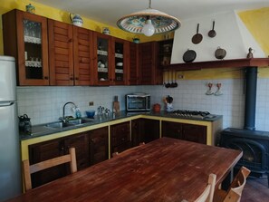 A kitchen with wooden cabinets, a gas stove, a sink, and a dining table. - Holiday Home 'Casa Centomila Volte Benvenuti' with Private Terrace (Tigliole)