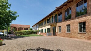 A brick building with a paved courtyard, a balcony, and a table with chairs.
