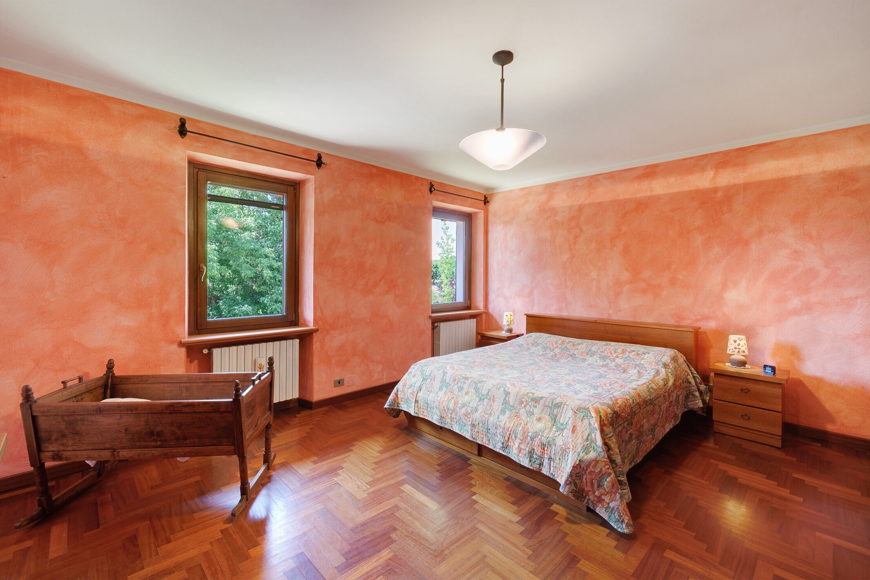 A bedroom with a wooden bed, two windows, a radiator, and a wooden chair.