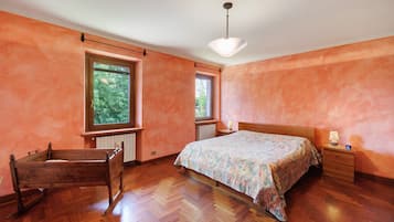 A bedroom with a wooden bed, two windows, a radiator, and a wooden chair.