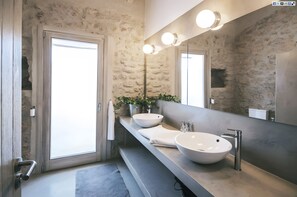 Een moderne badkamer met een stenen muur, twee wastafels, een grote spiegel en een deur.