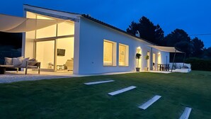 Una casa moderna con ventanas amplias, un patio con mobiliario exterior y un césped bien cuidado.