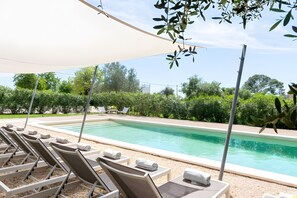 Ein Poolbereich mit Liegestühlen, einem Tisch und Sonnensegel.