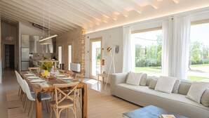 Un interior moderno con comedor, cocina y un amplio ventanal con vistas a zonas verdes.