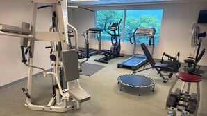Een sportschool met diverse fitnessapparaten, waaronder een loopband, elliptische trainer en losse gewichten.