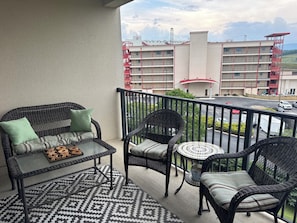 A balcony with wicker furniture, a patterned rug, and a view of a building with red fire escapes.