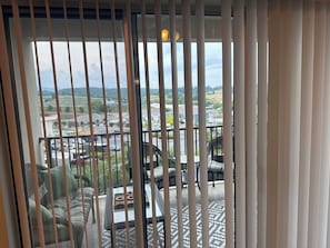 A balcony with wicker furniture, a glass table, and a view of a residential area.