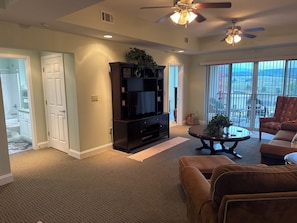 A living room with a TV, sofa, coffee table, and ceiling fans.