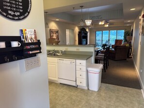 A modern kitchen with a dishwasher, a dining area with a table and chairs, and a living room with a couch.