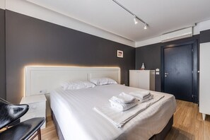 A modern hotel room with a large bed, bedside tables, a wardrobe, and a desk.
