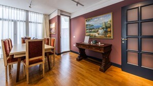 A dining area with a wooden table and chairs, a desk with a laptop, and a painting on the wall.