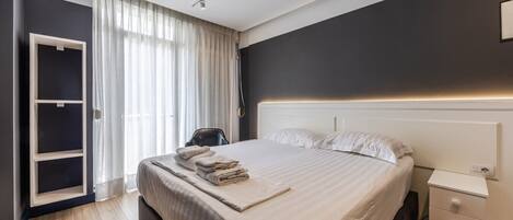 A modern hotel room with a large bed, a bedside table, a wardrobe, and a window with curtains.