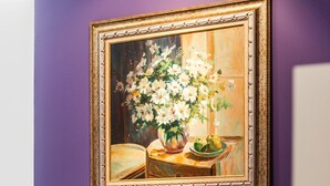 A room with two black leather chairs, a purple wall, and a framed painting of flowers.