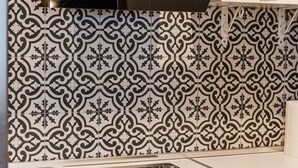 A kitchen with a black range hood, patterned backsplash, and a white countertop.