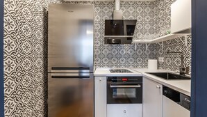Eine kompakte Küche mit Edelstahl-Kühlschrank, eingebautem Backofen und einer gestalterischen Spritzschutzwand.