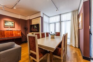 A dining area with a wooden piano, a television, and a large window with curtains.