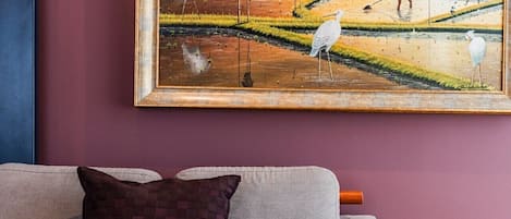 A living room with a sofa and a painting of a landscape.