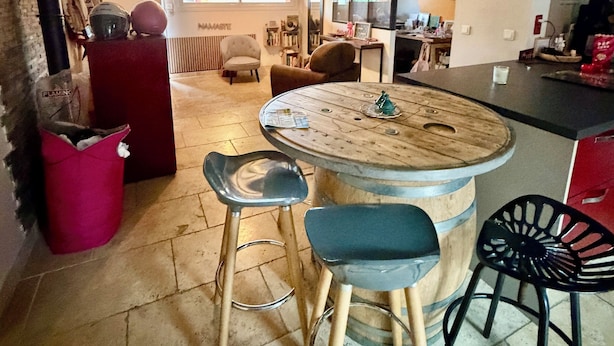 A kitchen with a round wooden table, two bar stools, a hanging light fixture, and a red cabinet. - Charming single-storey air-conditioned house, ideal for vacations in Provence (L'Isle-sur-la-Sorgue)