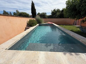 Ein rechteckiger Swimmingpool mit klarem Wasser, umgeben von einer niedrigen Steinmauer und Grünpflanzen.
