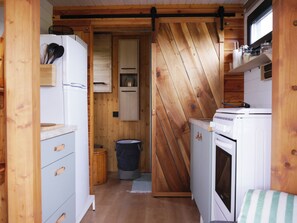 Une cuisine de taille réduite avec des murs en bois, un évier, une cuisinière et une poubelle.