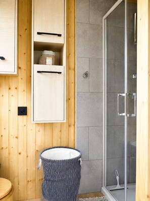 Une salle de bain aux murs lambrissés, équipée d’une douche, d’un porte-serviettes et de toilettes.