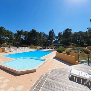 Ein rechteckiger Pool mit Fliesen umgeben, mit Liegestühlen und einer Holzterrasse.