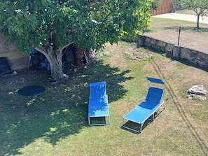 A backyard with two blue lawn chairs, a small table, and a tree providing shade.