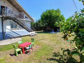 Une maison avec un escalier menant à un balcon, une cour gazonnée et du mobilier d’extérieur.