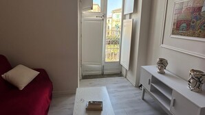 Ett litet rum med öppen planlösning, inrett med en röd soffa, ett vitt bord och ett vitt skåp.
