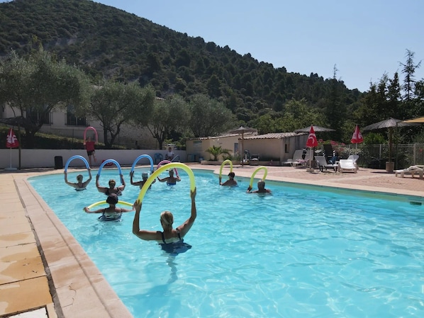 Ein Schwimmbecken mit Personen, die Schwimmreifen benutzen, umgeben von einer hügeligen Landschaft und Sitzgelegenheiten im Freien.