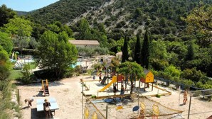 Un parque infantil con diversas estructuras de juego, incluyendo toboganes y zonas de escalada, rodeado de árboles y un paisaje montañoso.