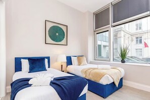 Habitació d'hotel amb dos llits, una finestra amb vista a edificis i una obra d'art emmarcada a la paret.