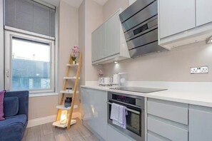 Cuina moderna amb forn integrat, taulell blanc i prestatgeria de fusta en forma d'escala.
