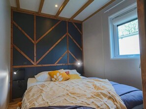A bedroom with a bed, a window, and a wall with wooden beams.