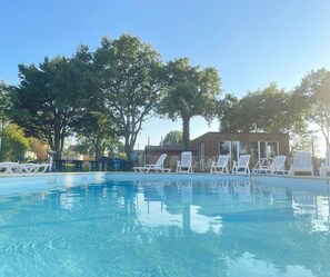 A swimming pool with lounge chairs, a wooden building, and trees in the background.