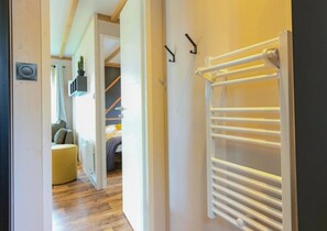 Un couloir avec un radiateur blanc, une porte donnant sur une chambre, et une petite plante accrochée au mur.