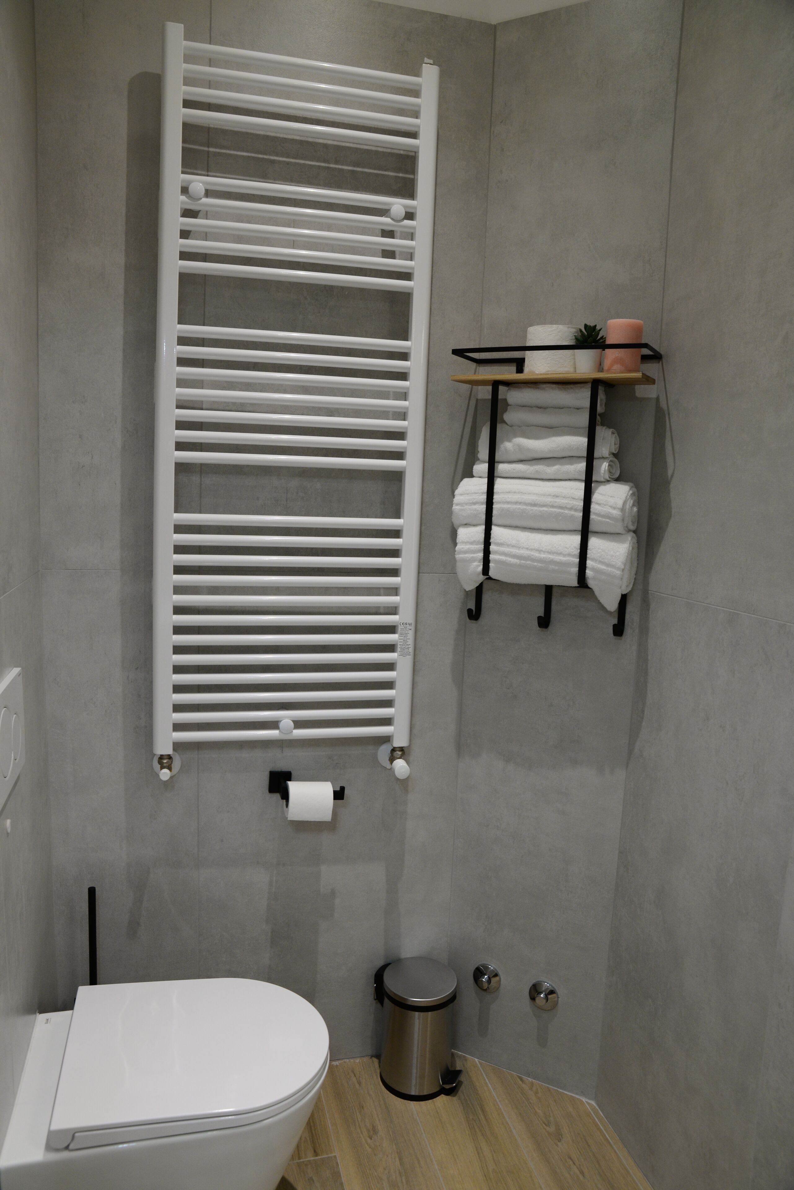 Ein Badezimmer mit Toilette, Handtuchhalter mit Handtüchern, Papierhalter und Mülleimer.