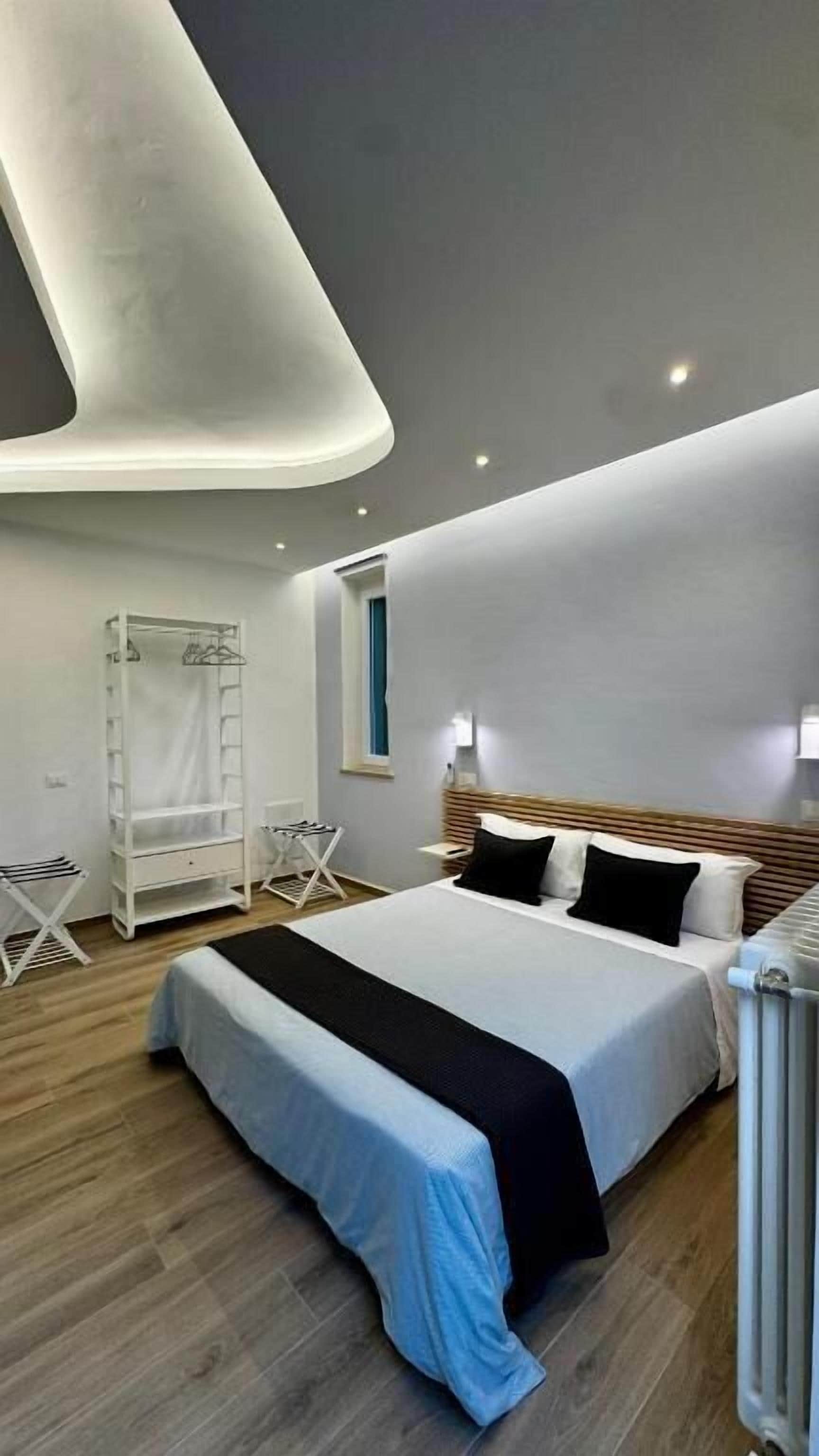 Un dormitorio moderno con una cama grande, un armario, una mesita y una lámpara en el techo.