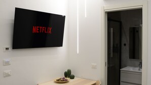 Une chambre moderne dotée d’une télévision à écran plat, d’une table à manger en bois, de chaises et d’une porte de douche en verre.