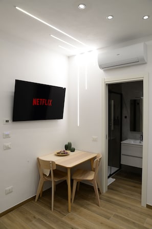 Ett modernt rum med en platt-TV, ett matbord i trÀ, stolar och en duschdörr i glas.