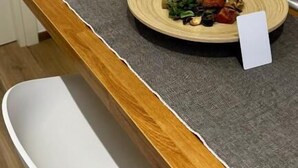 Une table à manger avec un set de table en fibres tressées, une assiette de nourriture et deux petites plantes en pot.