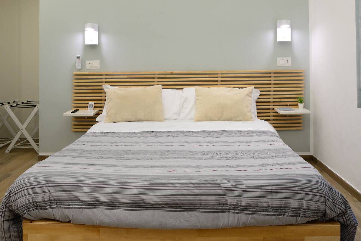 A modern bedroom with a wooden bed frame, a bedside table with a lamp, and a wall-mounted light fixture.