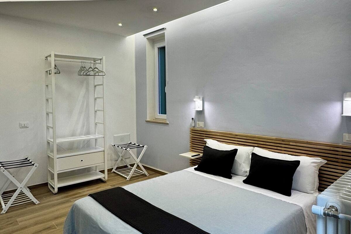 A modern bedroom with a bed, a wardrobe, a drying rack, and a radiator.