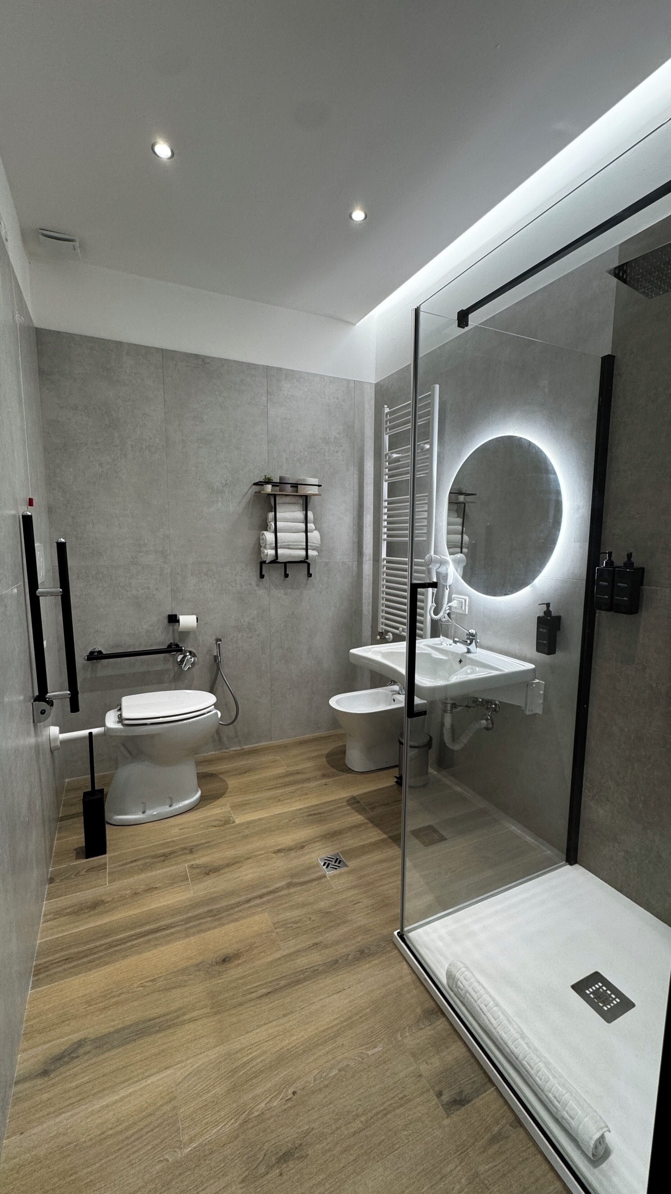 A modern bathroom with a glass shower enclosure, a round mirror, and a toilet with a bidet attachment.
