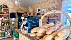 A bakery counter with baguettes, a cash register, and shelves with packaged goods. - Camping 4 étoiles - Piscine  - ccbgce0 (Sorgues)