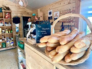 A bakery counter with baguettes, a cash register, and shelves with packaged goods. - Camping 4 étoiles - Piscine  - ccbgce0 (Sorgues)
