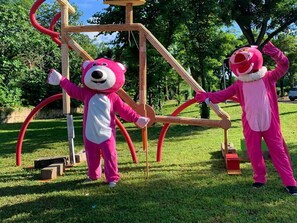 Two individuals in pink costumes standing in a grassy area with a wooden structure. - Camping 4 étoiles - Piscine  - ccbgce0 (Sorgues)
