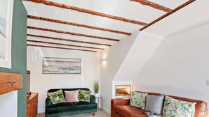 Ein Loft-Wohnzimmer mit freiliegenden Holzbalken, einem grünen Samtsofa, einem braunen Ledersofa und einem Bild an der Wand.