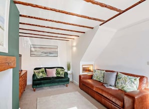 A loft-style living room with exposed wooden beams, a green velvet sofa, a brown leather sofa, and a painting on the wall. - Cottage Sleeps 5 With Parking and Garden (Amlwch)