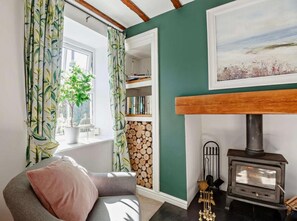 A cozy room with a fireplace, a bookshelf, and a window with curtains. - Cottage Sleeps 5 With Parking and Garden (Amlwch)
